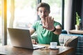 Wait, Stop! Young serious businessman in green t-shirt sitting, working on laptop, looking at camera, showing stop sign gesture