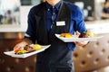 Waiter carrying two plates with meat dish on some festive event