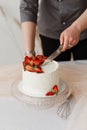 waiter cuts with a knife white cream cake with strawberries on the table