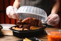 Waiter in gloves closing container with fresh prepared meal at wooden table, closeup. Food delivery service Royalty Free Stock Photo