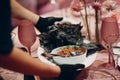 Waiter hands in gloves serving food for client. Food stylist decorate black food coronavirus protection in restaurant.