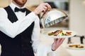 Waiter, hands and opening plate of food for serving, meal or customer service at indoor restaurant. Man employee caterer