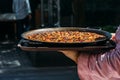 Waiter holding a giant Spanish paella dish outside a restaurant terrace