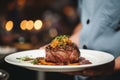 Waiter holding a plate with grilled beef steak with roasted vegetables on a side. Serving fancy food in a restaurant Royalty Free Stock Photo