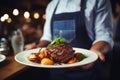 Waiter holding a plate with grilled beef steak with roasted vegetables on a side. Serving fancy food in a restaurant Royalty Free Stock Photo
