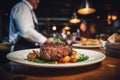 Waiter holding a plate with grilled beef steak with roasted vegetables on a side. Serving fancy food in a restaurant Royalty Free Stock Photo