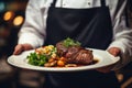 Waiter holding a plate with grilled beef steak with roasted vegetables on a side. Serving fancy food in a restaurant Royalty Free Stock Photo