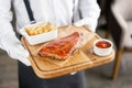 The waiter is holding a wooden plate Delicious Pork ribs. Full rack of ribs BBQ on wooden plate with french fries and Royalty Free Stock Photo