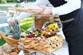 Waiter places food from one plate to another. Catering service. Wedding welcome food. Fruits on skewers and canapes.