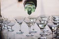 Waiter pouring martini in crystal glasses on table party at wedding reception. Martini row drinks at alcohol bar. Christmas and