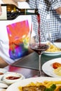 A waiter in a restaurant is pouring wine into wine glasses on a table at a party. There are blurry people attending the event in