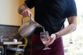 The waiter in the restaurant pours the water from the jug into the glass