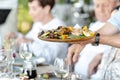 The waiter serves restaurant guests. The waiter holds a tray with food shrimp and vegetables Royalty Free Stock Photo