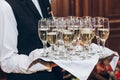 waiter serving stylish golden champagne in glasses on tray. elegant glasses of alcohol drinks serving at luxury wedding reception