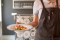 Waiter in uniform hurry to bring customers hot plate of tasty pasta inside modern restaurant