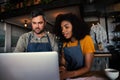 Waiter and waitress learning new menu off laptop drinking hot coffee standing in trendy cafe