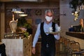 Waiter wearing face mask holding a tray with teas and going to serve the tables. New normal in restaurants.