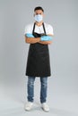 Waiter wearing medical face mask on light grey background