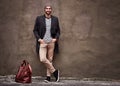 Waiting for her to show up. Shot of a handsome young man leaning against a wall outside in the city with his bag waiting Royalty Free Stock Photo