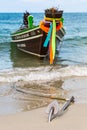 Waiting for passengers traditional Thai longtail boat with flowers and ribbons swinging on the waves, anchored on sandy beach.