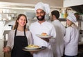 Waitress and crew of professional cooks posing at restaurant