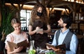 Waitress with face mask serving happy couple indoors in restaurant.