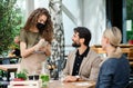 Waitress with face mask serving happy couple outdoors on terrace restaurant. Royalty Free Stock Photo