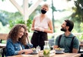 Waitress with face mask serving happy couple outdoors on terrace restaurant.