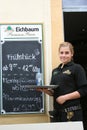 Waitress, Germany, standing by menu board.