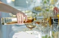 Waitress hand pouring cognac in wineglass from a bottle. Table served for party with dishes, bottles, wineglasses, fruits
