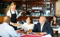 Waitress in mask serving cheerful people in pizzeria