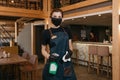 A waitress in a medical face mask is holding a bottle with sanitizer and a rag
