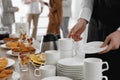 Waitress near table with dishware and different delicious snacks during coffee break, closeup