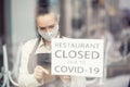 Waitress is sticking sign saying restaurant closed due to covid-19 on a window