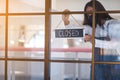 A waitress wearing protective face mask hanging closed sign on front door due to coronavirus effect