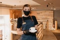 Waitress who wears a face mask and disposable gloves is serving a cup of coffee
