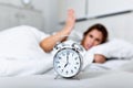 Wake up of an asleep girl stopping alarm clock on the bed in the morning. woman sleeping and wake up to turn off the alarm clock Royalty Free Stock Photo