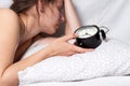 Wake up call. Young beautiful woman lying in bed and touching alarm clock. Girl doesn`t want to wake up