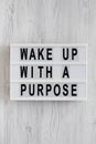 `Wake up with a purpose` words on a lightbox on a white wooden background, top view. Overhead, from above, flat lay. Close-up