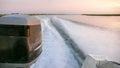 Wake and waves and close up of an outboard engine in coastal waters at sunset with marsh grass in the background