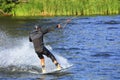 A wakeboarder rushes through the water at high speed along the green bank of the river Royalty Free Stock Photo