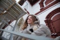 Walk around the city: the girl`s portrait in a gray short fur coat who stands behind handrail and looks in distance
