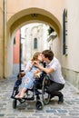 Walk in the city. Cheerful wheelchair girl kissing with her handsome boyfriend while spending time in love together.