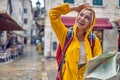 Walk in city in rain. Young tourist woman in raincoat with map, feeling happy, smiling. Travel in new city. Tourism, lifestyle,