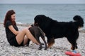 Young Caucasian woman is sitting and laughing on pebble beach with two dogs Bernese Mountain Dog and puppy of American Royalty Free Stock Photo