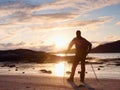 Walker watch sunny spring daybreak over sea. Hiker with backpack stand on sandy shore. Sun rays Royalty Free Stock Photo