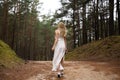 Walking Beautiful young blonde woman forest nymph in white dress in evergreen wood Royalty Free Stock Photo