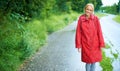 Walking the country roads on a rainy day. Gorgeous young blonde woman wearing a red raincoat in the rain outdoors on a Royalty Free Stock Photo