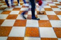 Walking, feet and legs blurred moving across orange and white check patterned marble floor