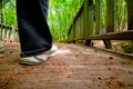 Walking in the forest. White sneakers girl trekking in forest. Wooden bridge.